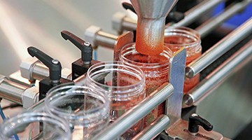 Red salsa being deposited into a glass jar at a manufacturers on a conveyor belt